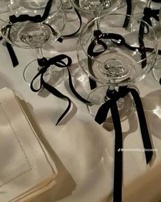 several wine glasses with black bows are on a white table cloth, ready to be served