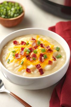 a bowl of potato soup with bacon, cheese and green onions on the side next to a spoon