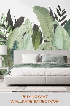 a bedroom with large green leaves on the wall and white bed in front of it