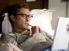 a man laying in bed while looking at an open book with a pencil in his mouth