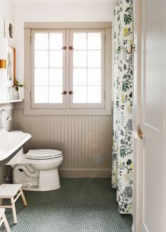 a white toilet sitting in a bathroom next to a sink and shower curtain with flowers on it