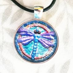 My tiny dragonfly painting is now available as a Photo Print Pendant!  I love our Mother Earth and the diversity of people, plants and animals. I strive to have all of my art reflects my environmental interest and my values.  🖤MATERIALS: They are 1 inch prints set into a round chrome bezel and covered with a round clear glass cabochon and comes on a black cord.  These are hand assembled chrome bezel with clear domed glass cabochon pendants Diameter: 1 Inch Comes with a black leather cord adjust Hand Painted Butterfly Jewelry Gift, Hand Painted Butterfly Jewelry For Gift, Unique Hand Painted Butterfly Jewelry, Adjustable Hand Painted Round Necklace, Adjustable Hand Painted Necklace, Adjustable Hand Painted Necklaces, Whimsical Artistic Jewelry For Gifts, Handmade Bohemian Dragonfly Necklace, Whimsical Artistic Design Jewelry Gift