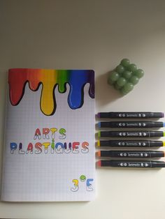 there is a notebook with the words art's plasticies written on it next to some crayons