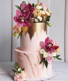 a pink and gold cake with flowers on top