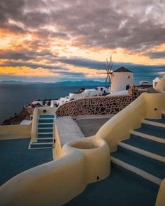 the sun is setting over some white buildings with blue steps leading up to them and a windmill in the distance