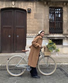 a woman standing next to a bike with flowers in the basket on the handlebars