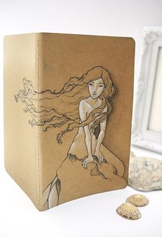 a box with a drawing of a mermaid on it and seashells next to it