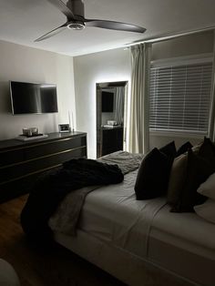 a bedroom with a bed, dresser and television on the wall next to it's windows