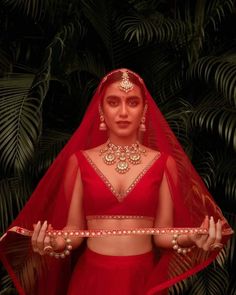 a woman in a red outfit holding a tray with jewelry on her hands and palm leaves behind her