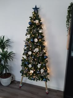 a small christmas tree with blue and silver ornaments on it, next to a potted plant