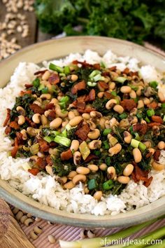 a bowl filled with rice, beans and greens on top of a wooden table next to vegetables