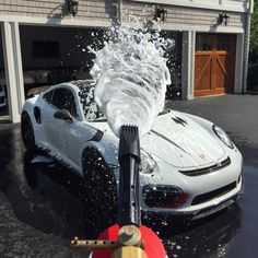 a white sports car being sprayed with water by a fire hydrant in front of a garage