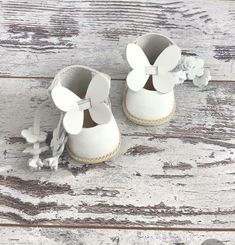 a pair of white baby shoes with bows on the front and bottom, sitting on a wooden floor