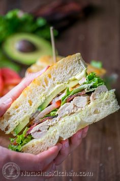 a person holding a sandwich with meat and veggies on it in their hands