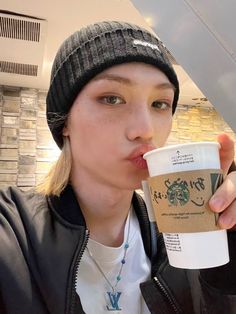 a woman in a beanie drinking out of a coffee cup with her tongue sticking out