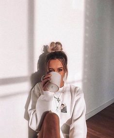 a woman sitting on the floor drinking from a cup