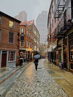 a person with an umbrella walks down a cobblestone street in the city on a rainy day