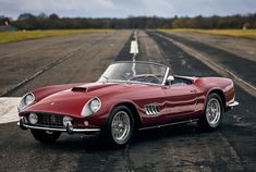 an old red sports car is parked on the road