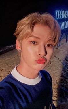 a young man with blonde hair and blue shirt posing for a photo in front of a neon sign