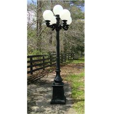 a black lamp post with three white lamps on it's sides in front of a fence