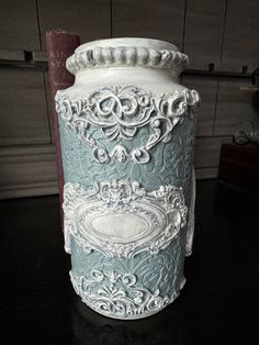 a white and blue vase sitting on top of a black table next to a wall