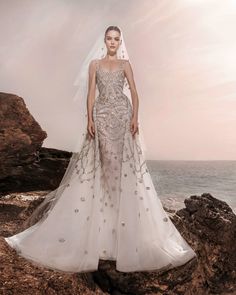 a woman in a wedding dress standing on rocks near the ocean