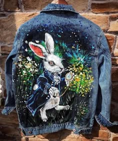 a denim jacket with an image of a rabbit on the back and flowers painted on it