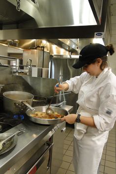 a woman cooking in a kitchen with pots and pans on the stove, while wearing a black hat