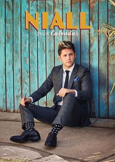 a man sitting on the ground in front of a wooden wall wearing a suit and tie