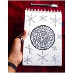 a hand holding a spiral notebook with snowflakes drawn on it and a pen next to it