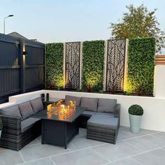 an outdoor fire pit on a patio surrounded by potted plants and seating area with privacy screens