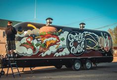 a man standing on a ladder next to a large truck with food painted on it