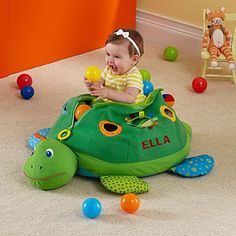 a baby sitting on top of a green turtle toy in a room filled with balls