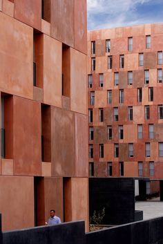 a man sitting on a bench in front of an orange building with many windows and balconies