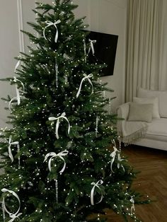 a decorated christmas tree in a living room with white lights and bows on it's branches