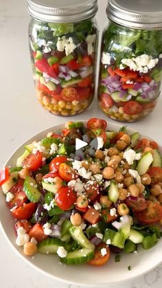 two mason jars filled with salad on top of a white table next to a plate