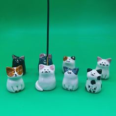 four ceramic cats sitting next to each other on a green surface with a black stick in the middle