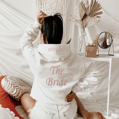 a woman sitting on top of a bed wearing a white hoodie with the words mrs santa monica printed on it