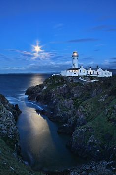 the lighthouse is lit up at night by the ocean