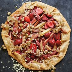 a pie topped with strawberries and other toppings on top of a black surface