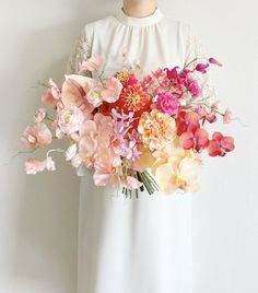 a woman in a white dress holding a bouquet of pink and orange flowers on her chest