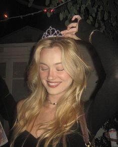 a woman wearing a tiara and smiling at the camera with her hair blowing in the wind