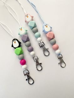 four different colored pacifiers with penguins attached to each one on a white surface