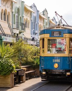 a blue and yellow train traveling down tracks next to tall buildings on either side of it