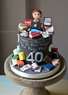 a birthday cake decorated with books and a boy on the top is made to look like he's using his laptop