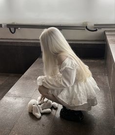 a woman with long white hair sitting on the ground next to a stuffed animal bear