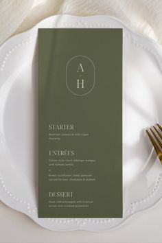 a white plate topped with a green menu card next to a gold fork and knife