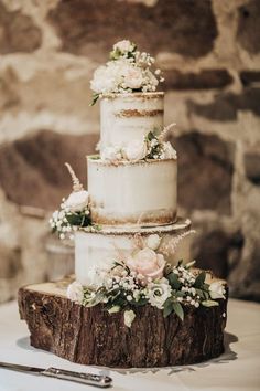 a three tiered wedding cake with flowers on top is sitting on a piece of wood