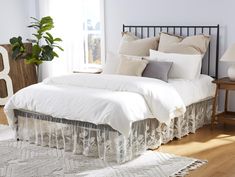 a bed with white linens and pillows in a bedroom next to a table with a potted plant on it