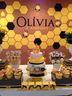 a table topped with cakes and cupcakes covered in frosting next to a honeycomb wall